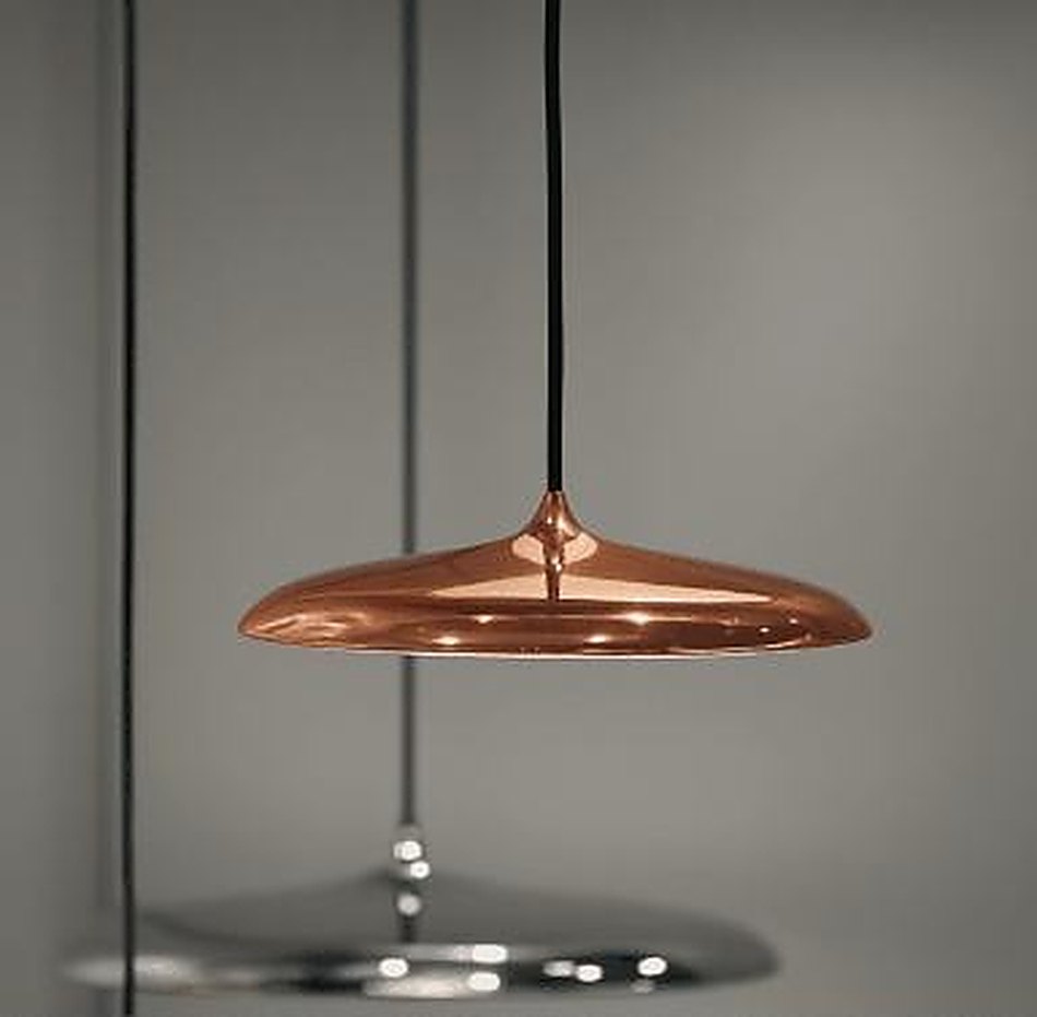 A polished copper disc pendant over a reflective surface