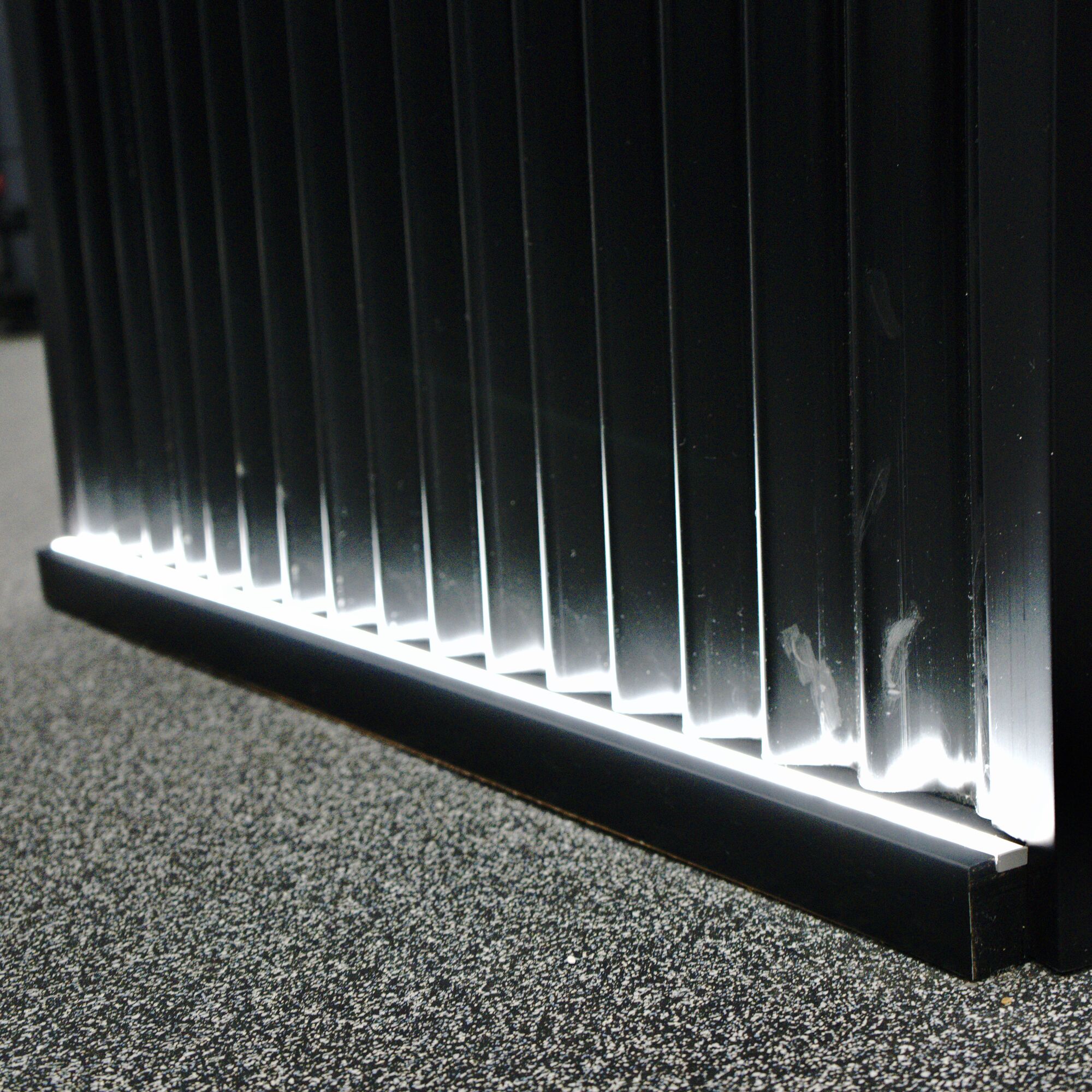 A fluted black wall washed by a floor-level LED line