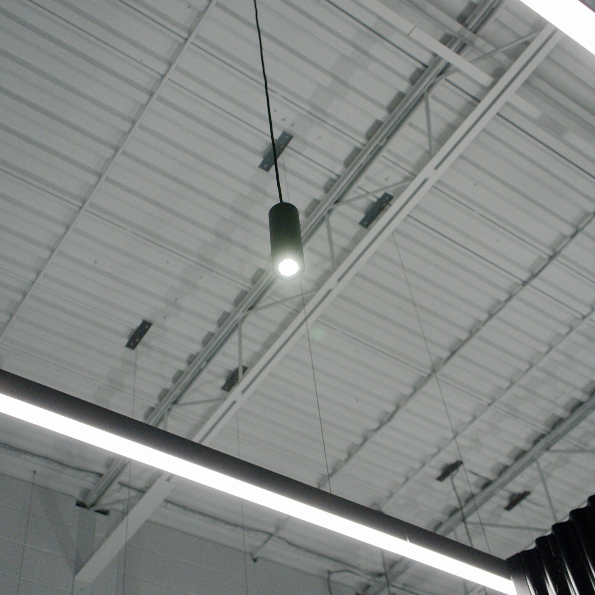 A linear light and a cylinder pendant installed under the steel deck at the Jeff Nippard studio