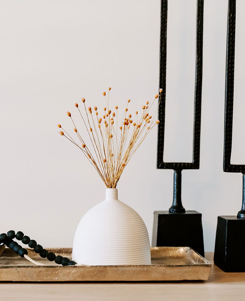 A white vase with flowers on top of a table.