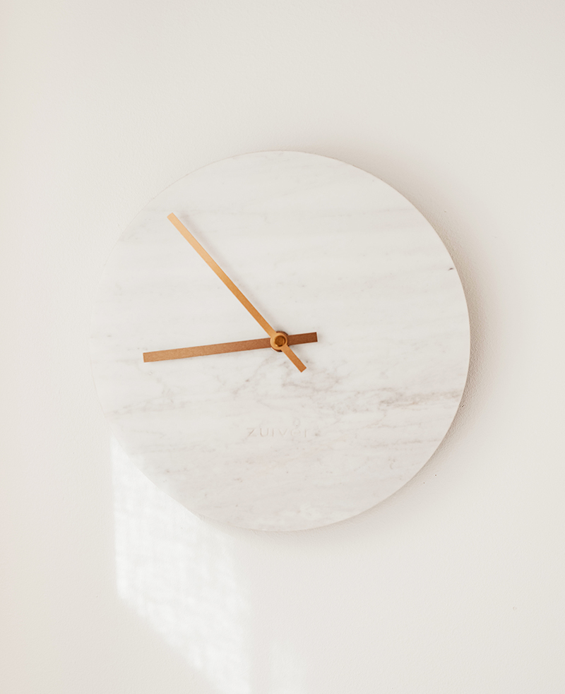 A white clock mounted to the side of a wall.